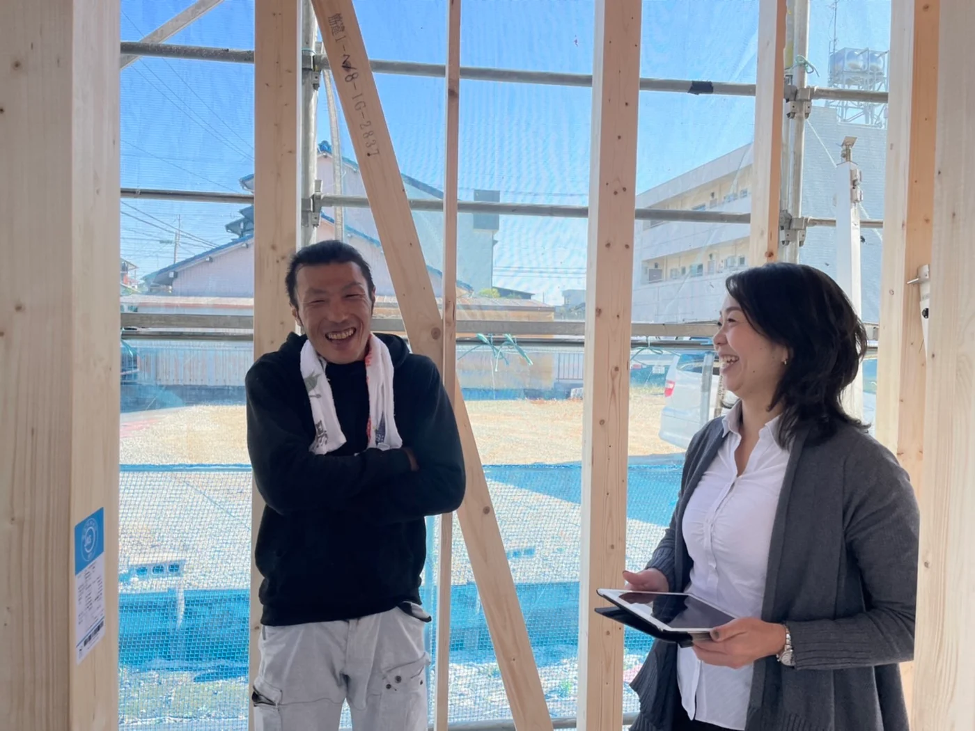 木造住宅の建築現場で、タブレットを手に笑顔で話す二人